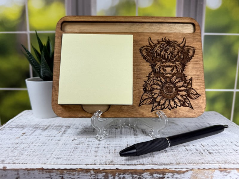 Wooden desk organizer with a cow and sunflower design, sticky notes, and a pen on a white surface. Sewing Bee Studio.