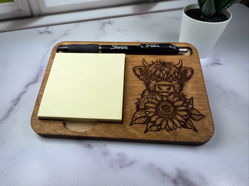 Wooden tray with engraved cow and sunflower design, sticky notes, and a pen on a marble surface. Sewing Bee & Laser Studio.