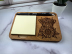 Wooden tray with engraved cow and sunflower design, sticky notes, and a pen on a marble surface. Sewing Bee & Laser Studio.