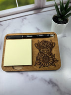 Wooden desk pad with engraved cow design, pen, and sticky notes on a marble surface. Sewing Bee & Laser Studio.