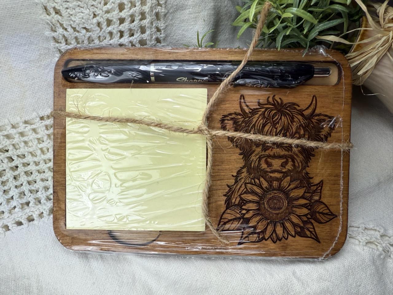 Wooden cutting board with laser-cut design of a highland cow and sunflower, tied with twine, on a textured surface. Shrink wrapped as mailed. Sewing Bee & Laser Studio.