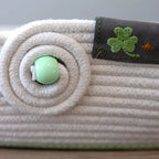 Close-up of a textured fabric item with a green button and embroidered shamrock on a gray background (Sewing Bee Studio)
