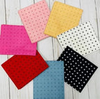 Collection of colorful fabric fat-quarters on a wooden surface. This "Kiss Hug" collection is sold by Sewing Bee Studio.