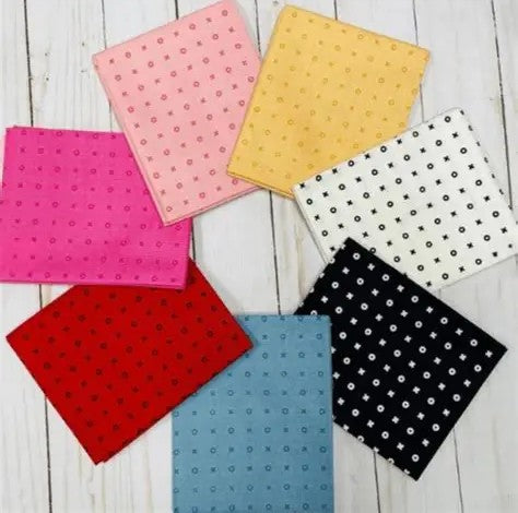 Collection of colorful fabric fat-quarters on a wooden surface. This "Kiss Hug" collection is sold by Sewing Bee Studio.
