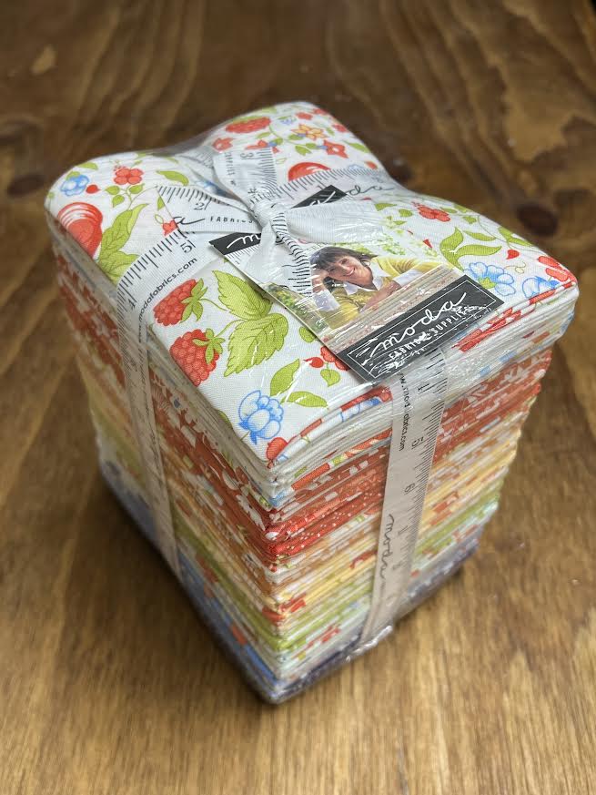 Bundle of fabric fat quarters with a visible brand label on a wooden display surface at Sewing Bee Studio.