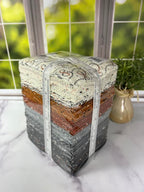 Stack of fabric squares with a measuring tape on a marble surface, blurred greenery in the background