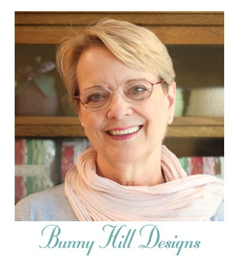 Designer, Anne Sutton, wearing glasses and a scarf with 'Bunny Hill Designs' text at the bottom. Her fat-eighths bundle, "I Believe in Angels" is sold by Sewing Bee Studio.