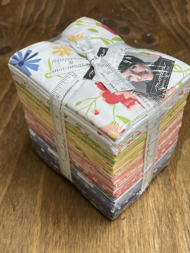 Bundle of fabric fat quarters with floral patterns on a wood display surface at Sewing Bee Studio.